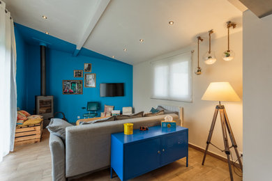 Modelo de salón abierto ecléctico con paredes azules, estufa de leña, suelo marrón, suelo de madera clara y televisor colgado en la pared