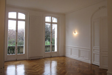 This is an example of a large traditional formal enclosed living room in Paris with white walls, light hardwood flooring, no fireplace, no tv and brown floors.