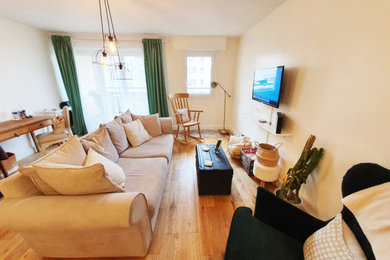 Diseño de salón abierto campestre grande con paredes beige, suelo de madera clara, televisor colgado en la pared y suelo marrón