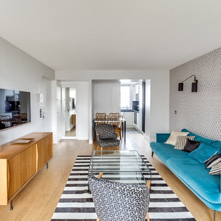 Aménagement d'un petit salon rétro ouvert avec un téléviseur fixé au mur, un mur blanc, un sol en bois clair, aucune cheminée et un sol marron.