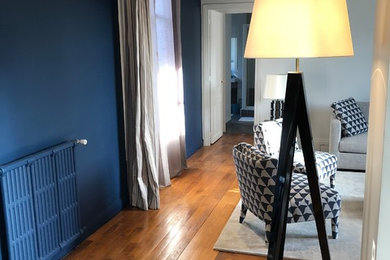 Cette image montre un grand salon traditionnel ouvert avec un mur bleu et un sol en bois brun.