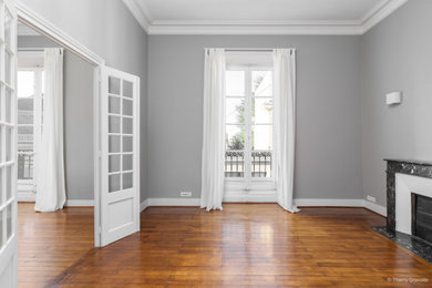 Exemple d'un grand salon chic avec un mur gris, parquet clair, une cheminée standard, un manteau de cheminée en pierre et un sol marron.