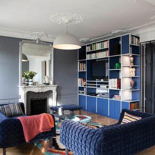 Cette photo montre un grand salon chic avec un mur gris, un sol en bois brun, une cheminée standard, un téléviseur fixé au mur et un sol marron.