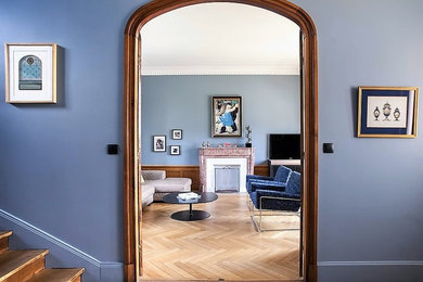 На фото: изолированная гостиная комната среднего размера в стиле неоклассика (современная классика) с синими стенами, светлым паркетным полом, стандартным камином, фасадом камина из камня, телевизором на стене и бежевым полом