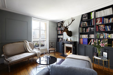Mid-sized eclectic enclosed medium tone wood floor living room library photo in Paris with gray walls, a standard fireplace and no tv
