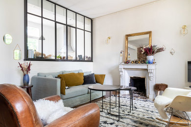 パリにあるお手頃価格の中くらいなエクレクティックスタイルのおしゃれなLDK (白い壁、淡色無垢フローリング、標準型暖炉、石材の暖炉まわり、据え置き型テレビ、茶色い床) の写真