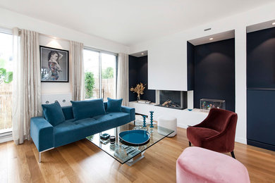 Inspiration pour un grand salon design ouvert avec un mur bleu, parquet clair, cheminée suspendue, un manteau de cheminée en plâtre, aucun téléviseur et un sol blanc.