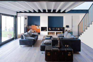 Exemple d'un grand salon tendance fermé avec un mur bleu, une bibliothèque ou un coin lecture, parquet clair, une cheminée standard, un manteau de cheminée en pierre et un sol beige.