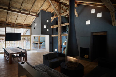 Diseño de salón actual con paredes negras, suelo de madera en tonos medios, chimeneas suspendidas, marco de chimenea de metal y televisor retractable