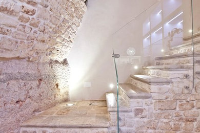 Immagine di una piccola scala a "L" design con pedata in pietra calcarea, alzata in pietra calcarea e parapetto in vetro