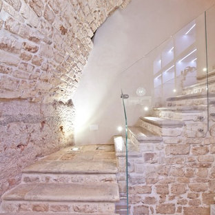 Immagine di una piccola scala a "L" design con pedata in pietra calcarea, alzata in pietra calcarea e parapetto in vetro