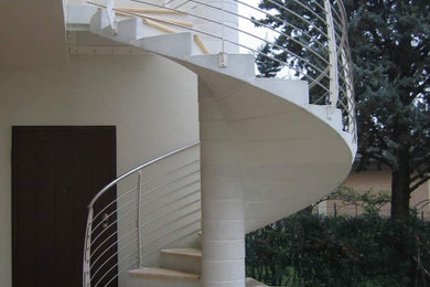 Diseño de escalera de caracol contemporánea con escalones de mármol, contrahuellas de hormigón y barandilla de metal