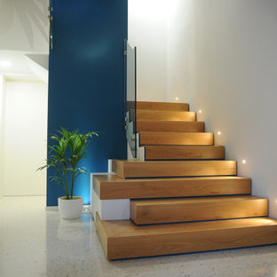 Esempio di una grande scala a "L" minimal con pedata in legno, alzata in legno e parapetto in vetro