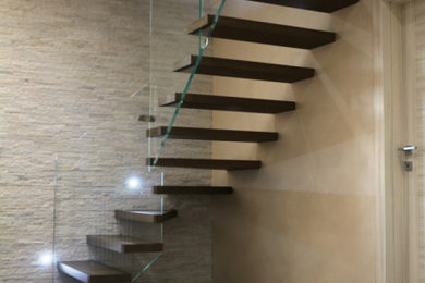 Imagen de escalera en L minimalista sin contrahuella con escalones de madera y barandilla de vidrio