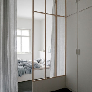 Modelo de dormitorio principal, minimalista, de tamaño medio, con paredes blancas, suelo de madera oscura, estufa de leña, marco de chimenea de baldosas y/o azulejos y suelo negro