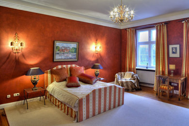 Großes Klassisches Hauptschlafzimmer mit roter Wandfarbe und braunem Holzboden in Berlin