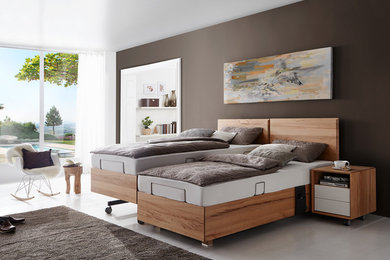 Imagen de dormitorio principal actual de tamaño medio sin chimenea con paredes marrones, suelo de madera clara, suelo blanco y marco de chimenea de madera