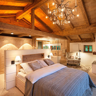 Modelo de dormitorio principal, campestre, de tamaño medio, con paredes blancas, suelo de madera clara, chimenea de esquina, marco de chimenea de yeso y suelo marrón