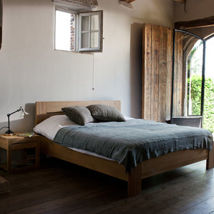 Imagen de dormitorio urbano, grande, con paredes blancas, suelo de madera oscura, chimenea tradicional y marco de chimenea de piedra