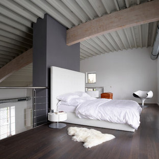 Ejemplo de dormitorio tipo loft, industrial, extra grande, sin chimenea, con suelo de madera oscura, paredes blancas, marco de chimenea de yeso y suelo marrón