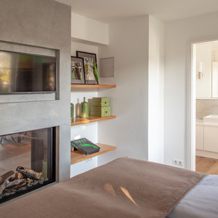 Diseño de habitación de invitados actual, de tamaño medio, con paredes blancas, suelo de madera pintada, chimenea de doble cara y marco de chimenea de hormigón
