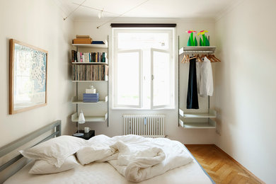 Kleines Modernes Schlafzimmer ohne Kamin mit weißer Wandfarbe und braunem Holzboden in München