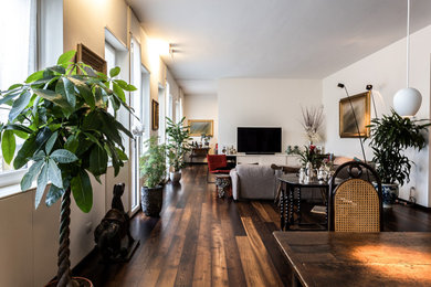 Imagen de sala de estar abierta moderna con paredes blancas, suelo de madera oscura, televisor colgado en la pared y suelo marrón