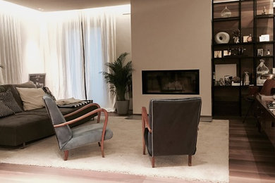 Foto de sala de estar abierta actual pequeña con paredes blancas, suelo de madera clara, chimenea lineal, marco de chimenea de yeso y televisor colgado en la pared