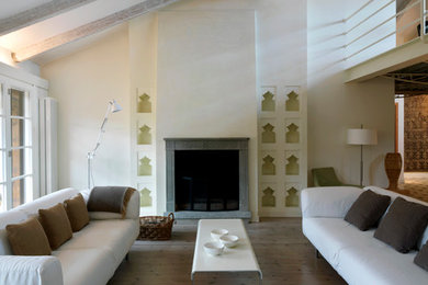 Modelo de salón abierto mediterráneo grande con paredes blancas, suelo de madera clara, todas las chimeneas y marco de chimenea de piedra