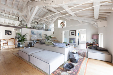 Modelo de sala de estar tipo loft mediterránea extra grande sin chimenea y televisor con paredes blancas, suelo de madera clara y suelo beige