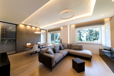 Ejemplo de salón para visitas abierto actual extra grande con paredes blancas, suelo de madera clara, televisor colgado en la pared y suelo beige