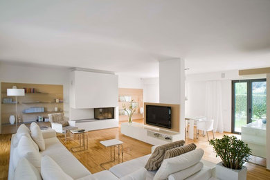 Ejemplo de salón abierto actual de tamaño medio con paredes blancas, suelo de madera clara, chimenea lineal, marco de chimenea de yeso y televisor colgado en la pared