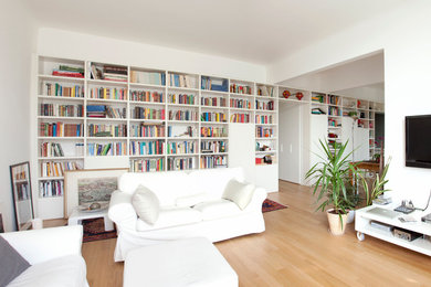 Ispirazione per un grande soggiorno design aperto con libreria, pareti bianche, pavimento in legno massello medio e TV a parete