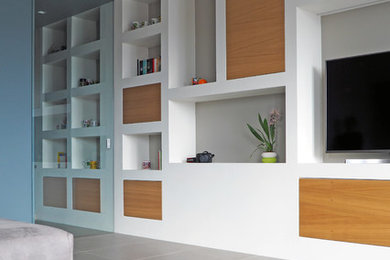 Imagen de biblioteca en casa abierta moderna de tamaño medio con paredes blancas, suelo de baldosas de cerámica, televisor colgado en la pared y suelo gris