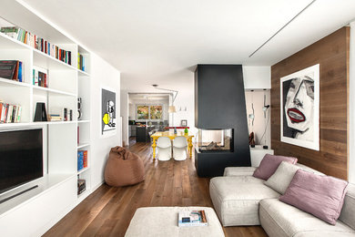 Immagine di un soggiorno moderno con pareti bianche, parquet chiaro, camino bifacciale, cornice del camino in metallo e TV a parete