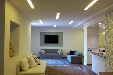 Modelo de salón con barra de bar cerrado moderno con paredes beige, suelo de madera en tonos medios y televisor colgado en la pared