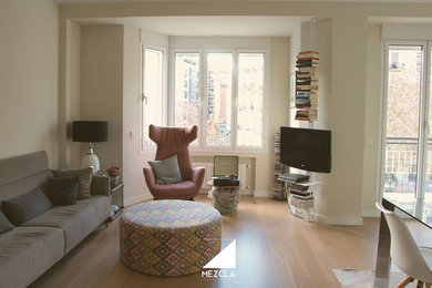 Immagine di un soggiorno minimalista di medie dimensioni e aperto con libreria, pareti beige, parquet chiaro e porta TV ad angolo
