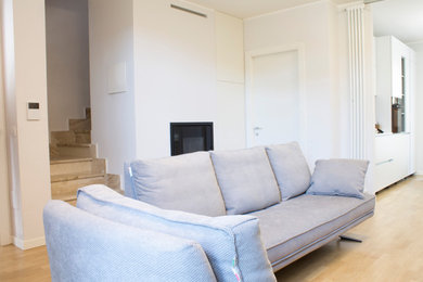 Modelo de salón abierto minimalista de tamaño medio con paredes grises, suelo de madera clara, estufa de leña y marco de chimenea de yeso