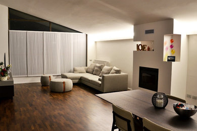 Esempio di un ampio soggiorno contemporaneo aperto con pareti bianche, parquet scuro, stufa a legna, cornice del camino in intonaco e pavimento marrone