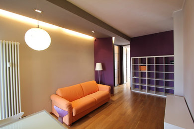 Imagen de sala de estar con biblioteca abierta actual de tamaño medio con paredes púrpuras, suelo de madera en tonos medios, televisor colgado en la pared y suelo beige