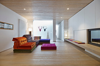 Foto di un grande soggiorno minimal aperto con pareti bianche, parquet chiaro, camino lineare Ribbon e cornice del camino in intonaco