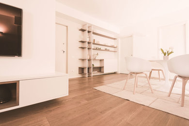Diseño de biblioteca en casa abierta moderna grande con paredes blancas, suelo de madera clara, televisor colgado en la pared y suelo gris