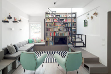 Modelo de sala de estar con biblioteca contemporánea sin chimenea con paredes blancas, suelo de madera clara y pared multimedia