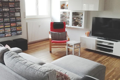 Idee per un soggiorno minimalista di medie dimensioni e aperto con libreria, pareti bianche, pavimento in legno massello medio, TV autoportante e pavimento multicolore