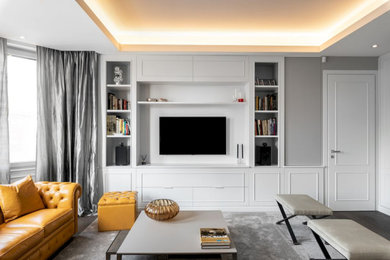 Modelo de biblioteca en casa abierta actual con paredes grises, suelo de madera oscura y televisor colgado en la pared