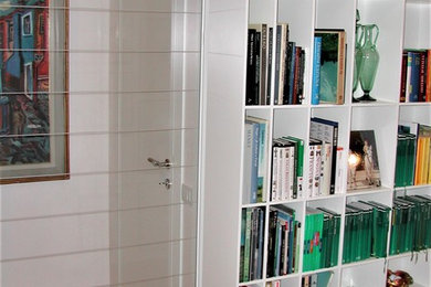 Ispirazione per un soggiorno design di medie dimensioni e chiuso con libreria, pareti bianche, pavimento in legno massello medio e pavimento beige