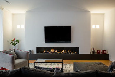 トゥーリンにある中くらいなコンテンポラリースタイルのおしゃれなリビング (グレーの壁、淡色無垢フローリング、横長型暖炉、壁掛け型テレビ、茶色い床) の写真