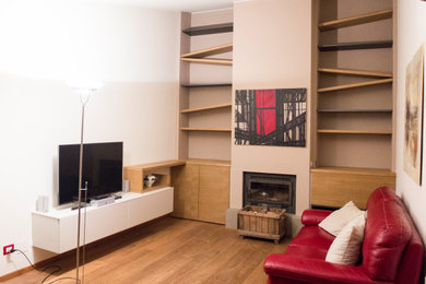 Imagen de biblioteca en casa abierta actual de tamaño medio con paredes blancas, suelo de madera en tonos medios, estufa de leña y televisor colgado en la pared
