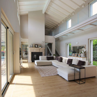 Foto di un ampio soggiorno country aperto con libreria, camino bifacciale, cornice del camino in pietra ricostruita, travi a vista, soffitto a volta, pannellatura, pareti grigie, parquet chiaro e pavimento beige