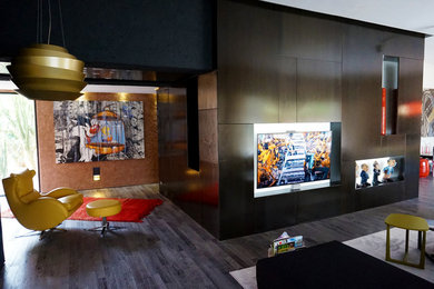 Modelo de salón abierto industrial con paredes multicolor, suelo de madera oscura, marco de chimenea de metal, televisor colgado en la pared y suelo multicolor